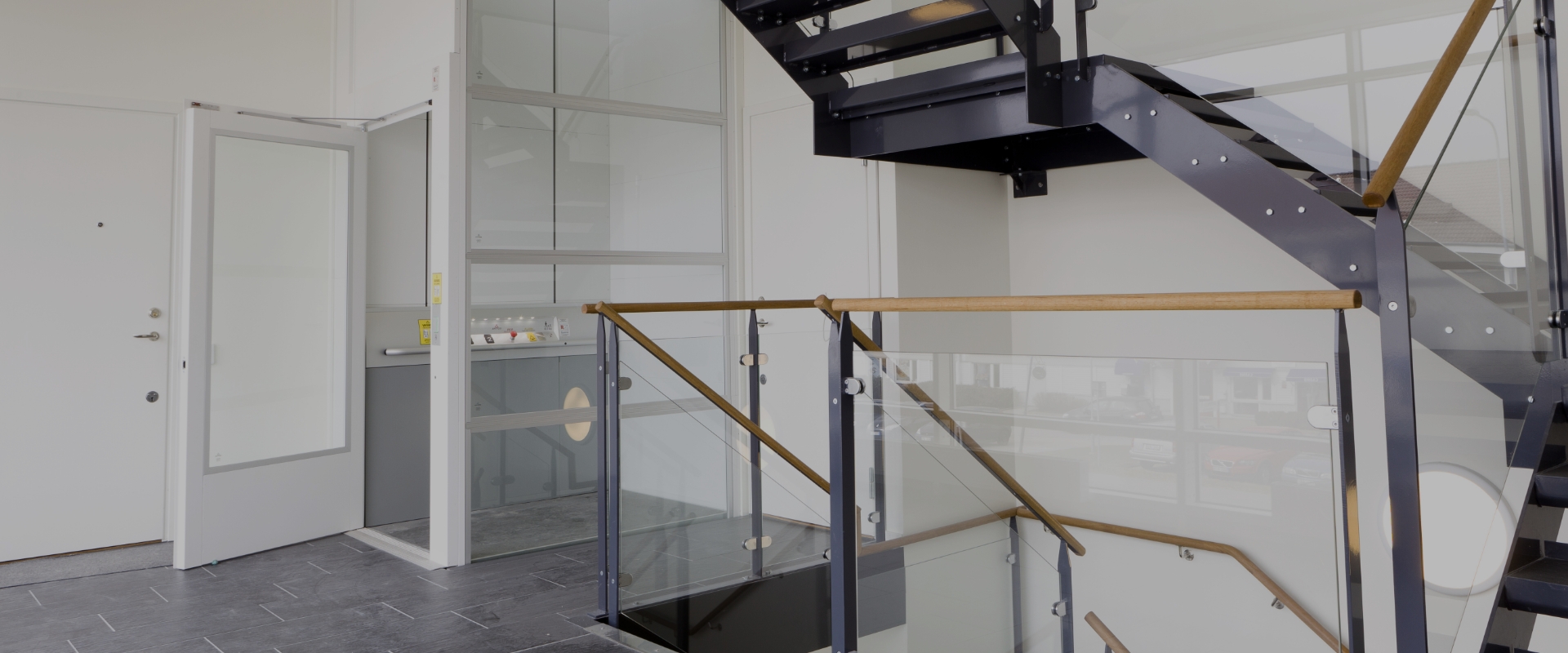 Titelbild für "Öffentliche Lifte" Weiträumiger Flur in einem öffentlichen Gebäude mit moderner Treppe und weißem Fahrstuhl